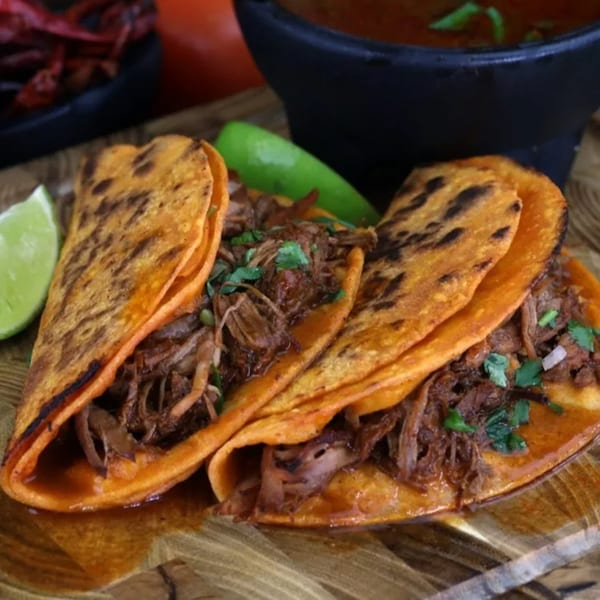 Three Pika Tortas Ahogadas birria tacos with lime wedges and a bowl of consommé.