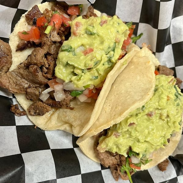 Two Pika Tortas Ahogadas tacos with steak, pico de gallo, and guacamole on checkered paper.