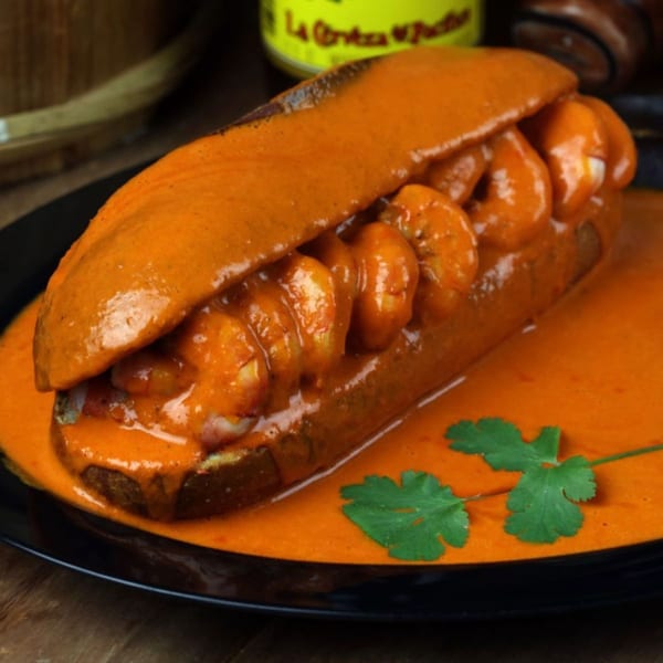 A Pika Tortas Ahogadas shrimp torta, drenched in a vibrant orange sauce, garnished with cilantro.