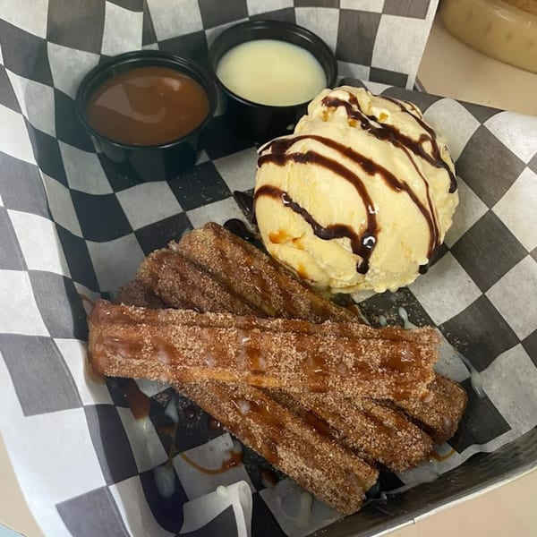 Churros with cinnamon sugar, caramel drizzle, vanilla ice cream with chocolate syrup, and two dipping sauces.