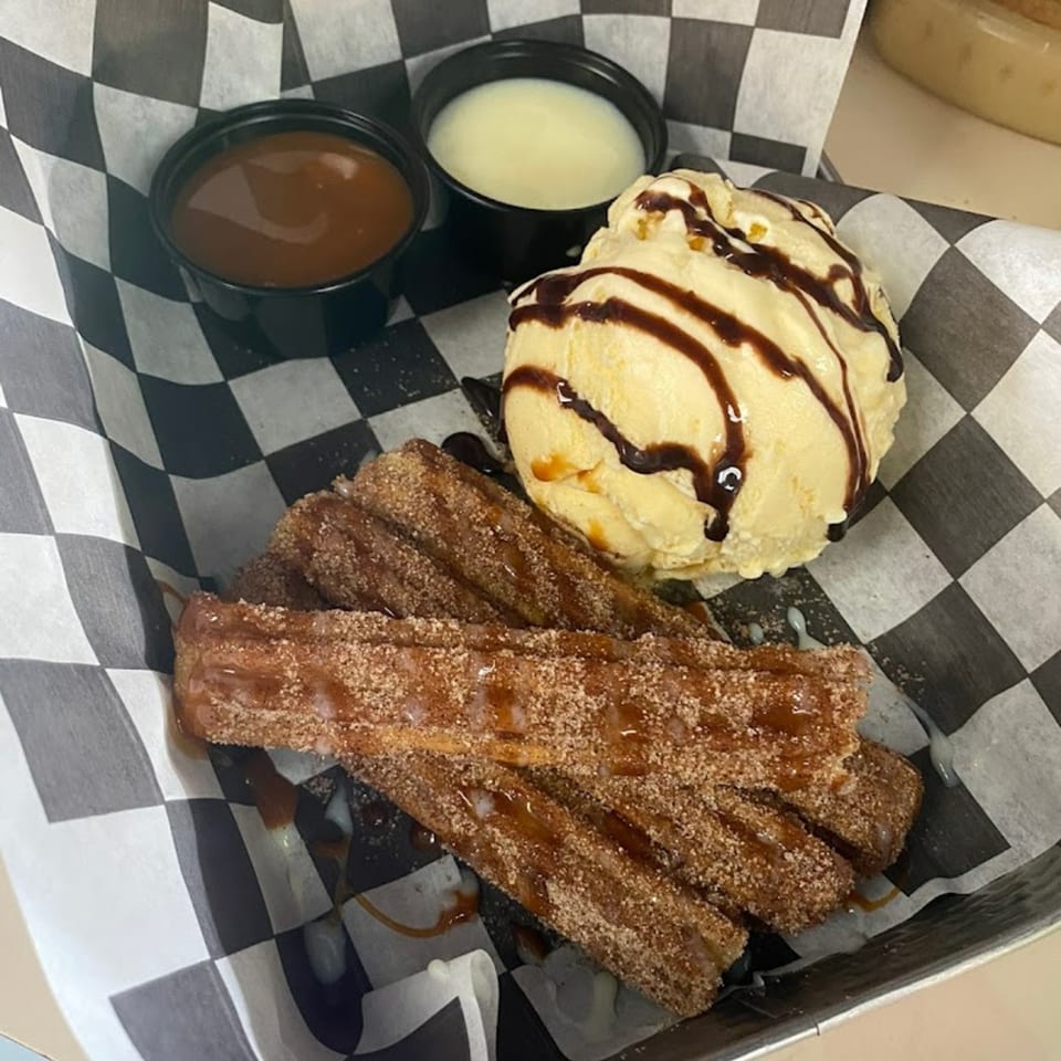 Churros with cinnamon sugar, caramel drizzle, vanilla ice cream with chocolate syrup, and two dipping sauces.
