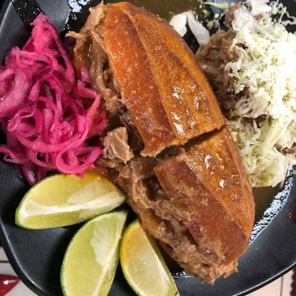 Pika Tortas Ahogadas' torta ahogada with pickled red onions, shredded cabbage, cheese, and lime wedges.