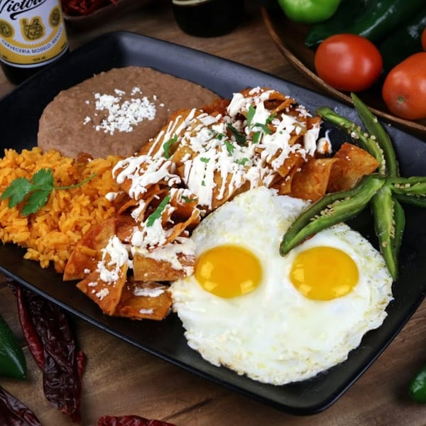 Mexican breakfast plate with chilaquiles, two fried eggs, refried beans, and rice.